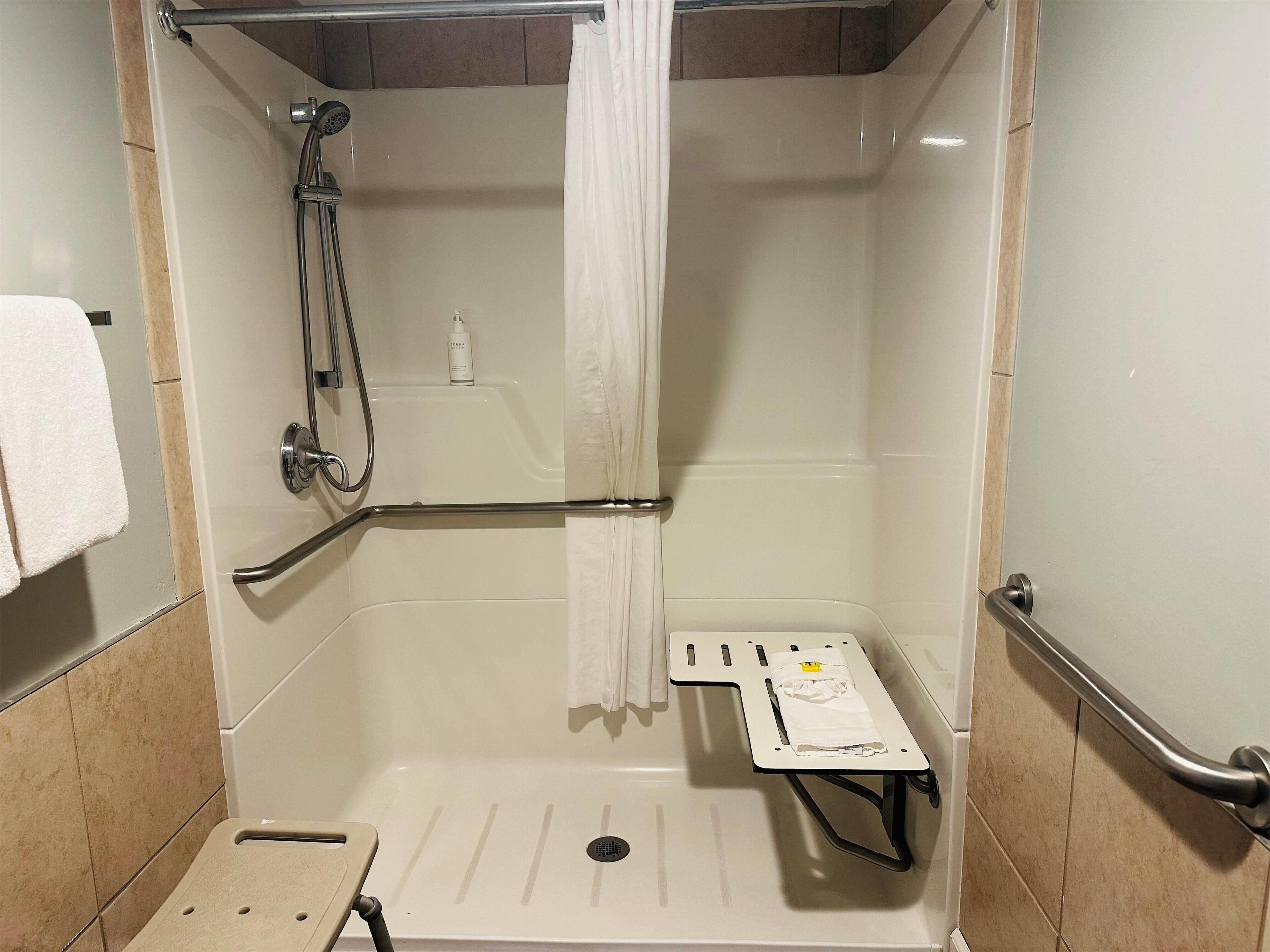 A shower stall with a handheld showerhead, a grab bar, and a small shelf with a towel.