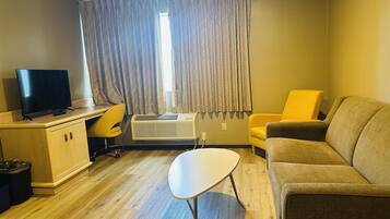Una habitación pequeña y amoblada, con escritorio, televisor, sofá y ventana con cortinas.