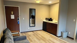 A compact living space with a kitchenette, a sofa, a mirror, and a door with a light switch. - Days Inn by Wyndham Seatac Airport (SeaTac)