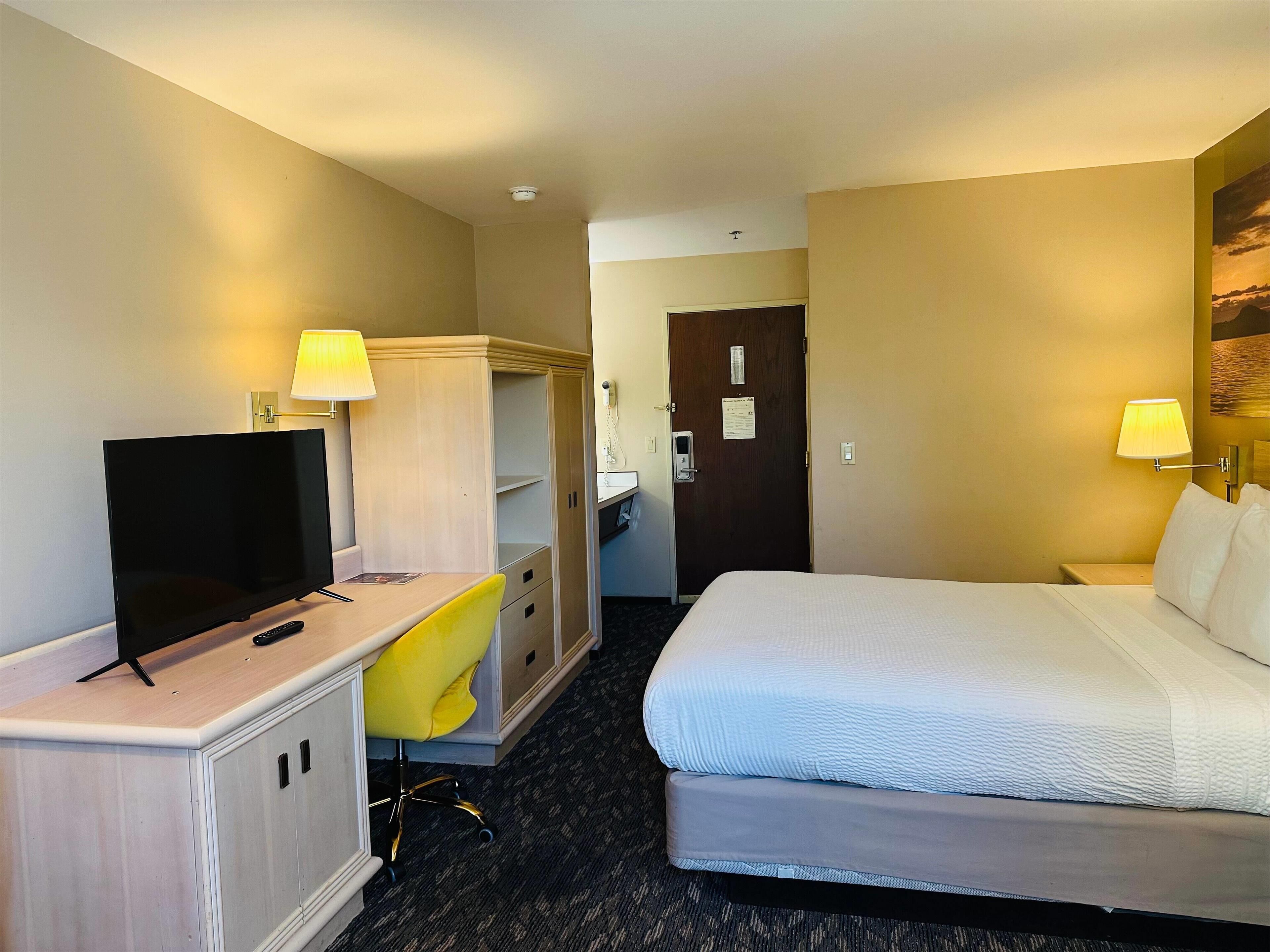 A hotel room with a bed, a desk with a TV, a chair, a wardrobe, and a door.