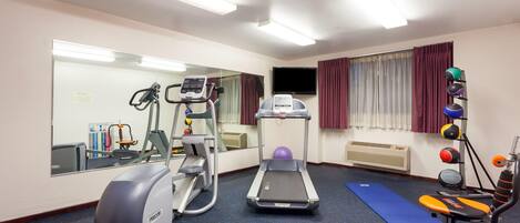 A gym with exercise equipment including treadmills, an elliptical, and a stationary bike. There is a mirror, a television, and a window with curtains.