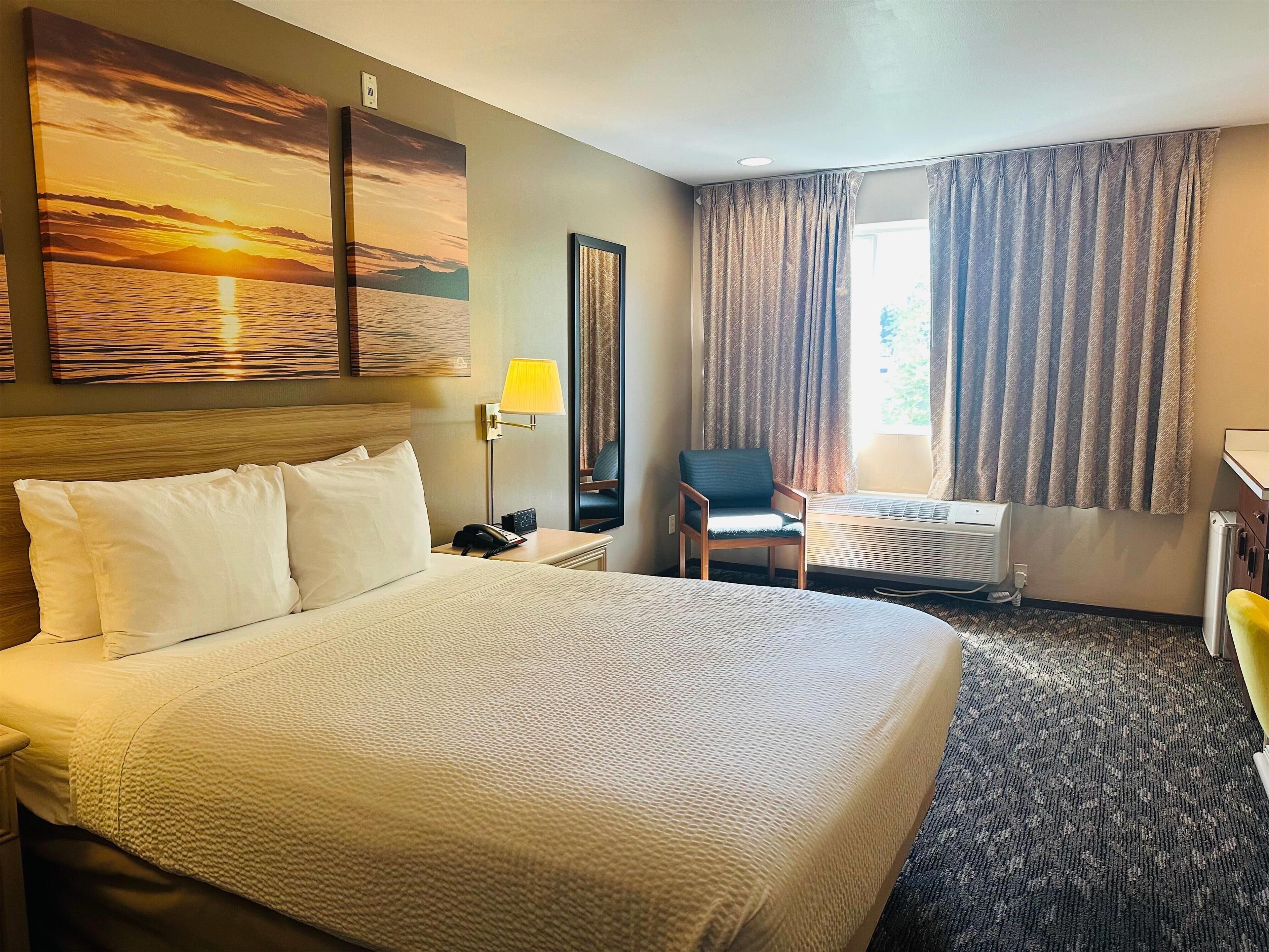 A hotel room with a large bed, a chair, a desk, and a window with curtains.