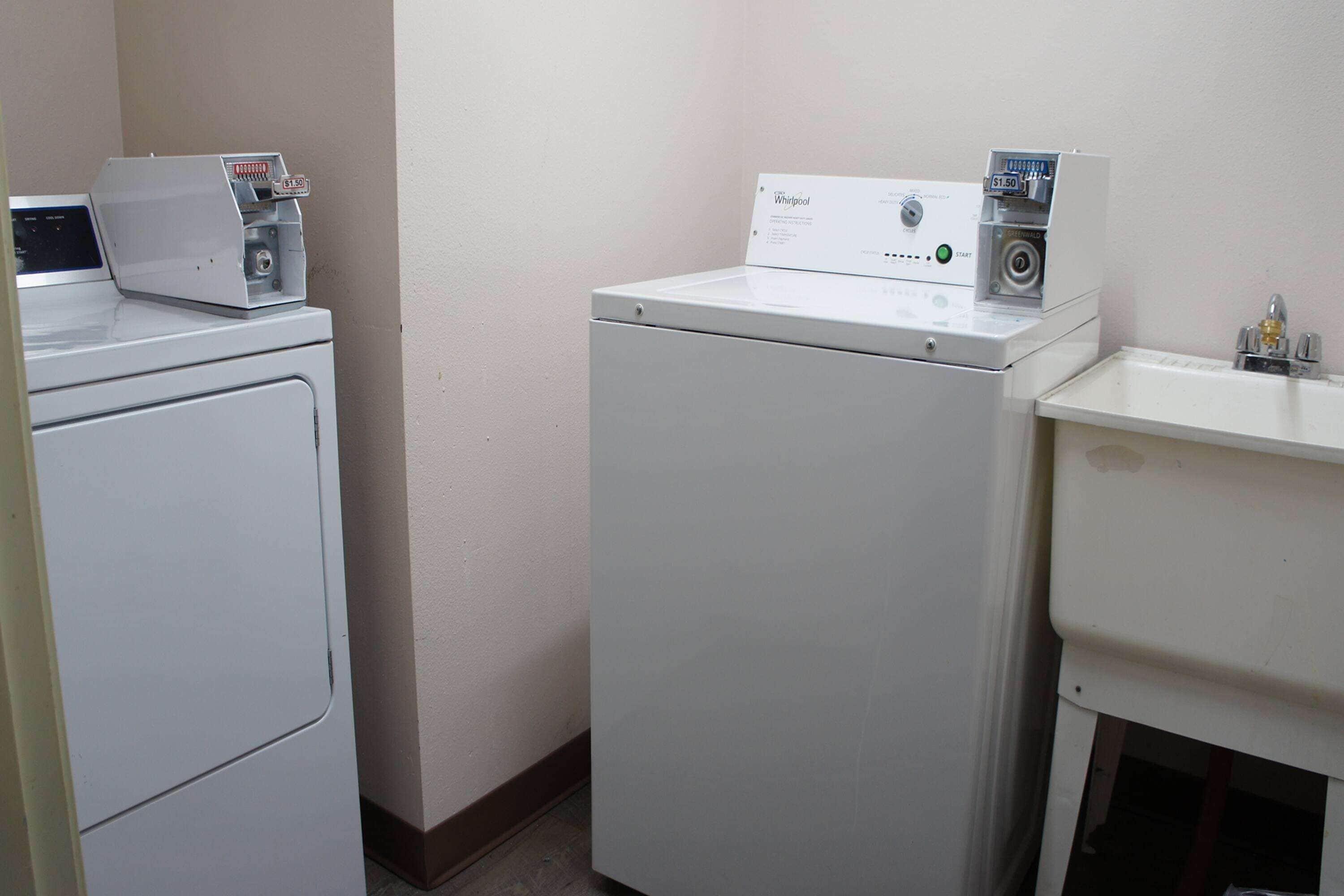 A laundry room with two white washers and dryers, a small sink, and a control panel on the dryers.
