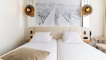 A double bed with white linens, two bedside tables, a chair, and a wall-mounted artwork of a vineyard.