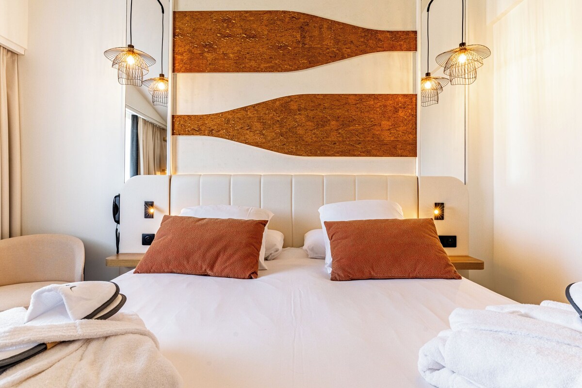 A modern hotel room with a large bed, two side tables, a telephone, and a wall-mounted light fixture.