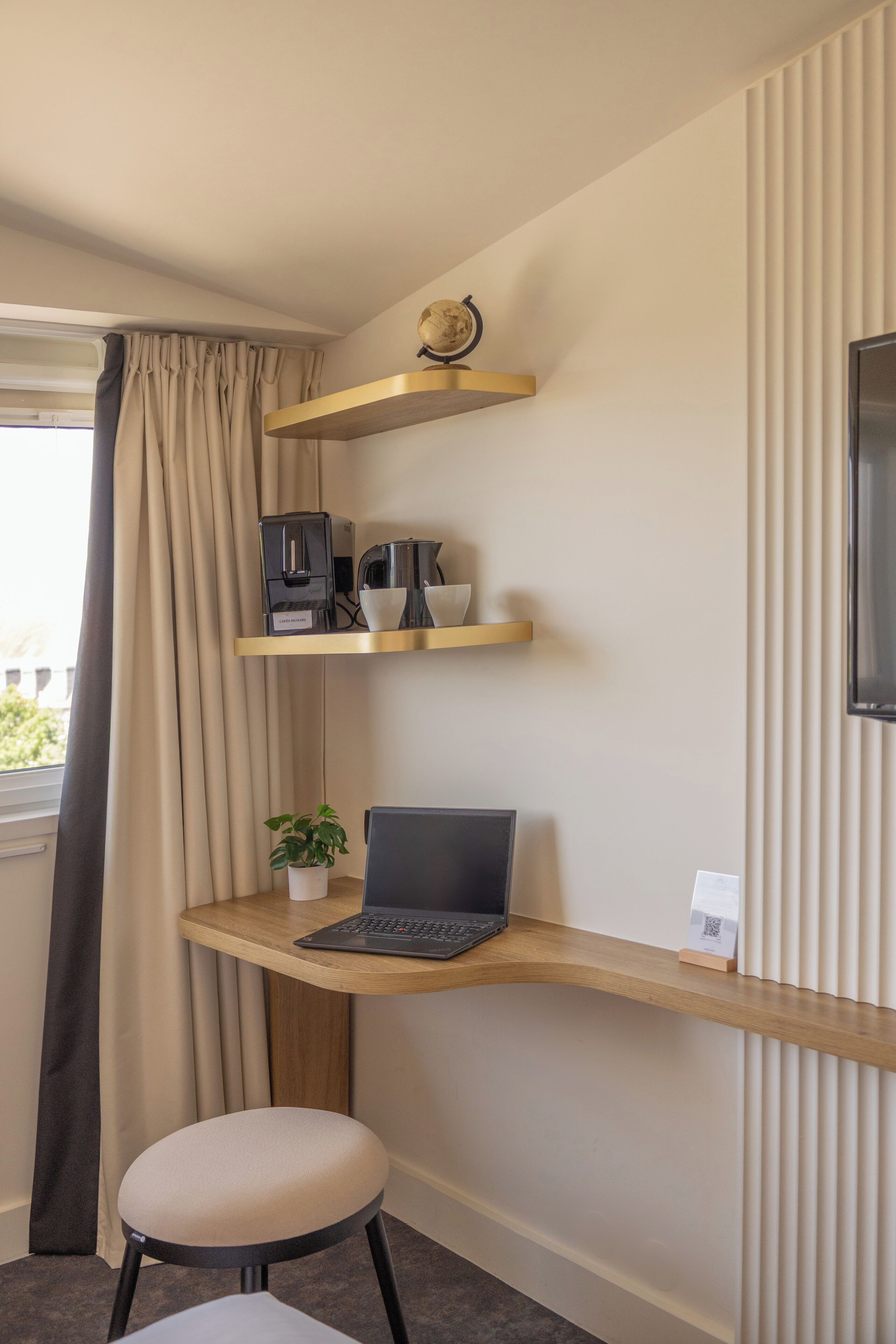 A modern hotel room with a curved desk, a laptop, a coffee maker, and a globe on a shelf.