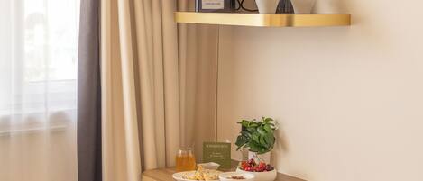 A kitchenette with a coffee maker, cups, a bowl of fruit, and a plant on a wooden shelf.