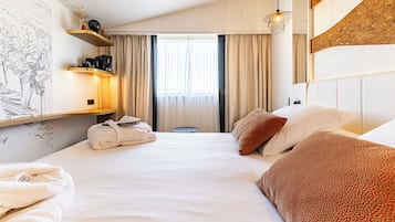 Ein Hotelzimmer mit Bett, Nachttisch, Lampe, einem Fenster mit Vorhängen und einer Wand mit einem dekorativen Element.
