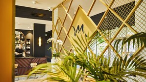A modern interior with a bar area, seating, and a decorative plant in the foreground. - Mercure Beaune Centre (Beaune)