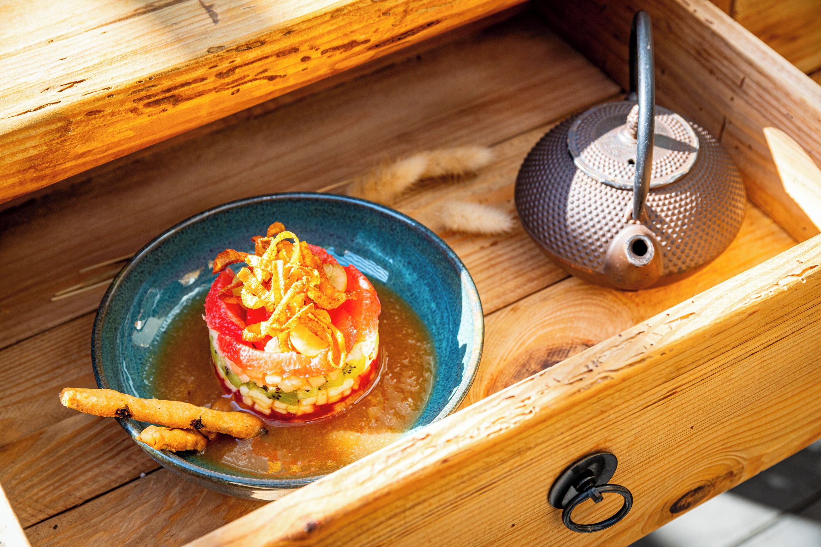 A wooden tray with a blue bowl containing a dish and a teapot.