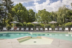 A swimming pool with lounge chairs and umbrellas, surrounded by trees.