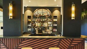 A bar area with a bartender, a well-stocked liquor shelf, and two stools. - Mercure Beaune Centre (Beaune)