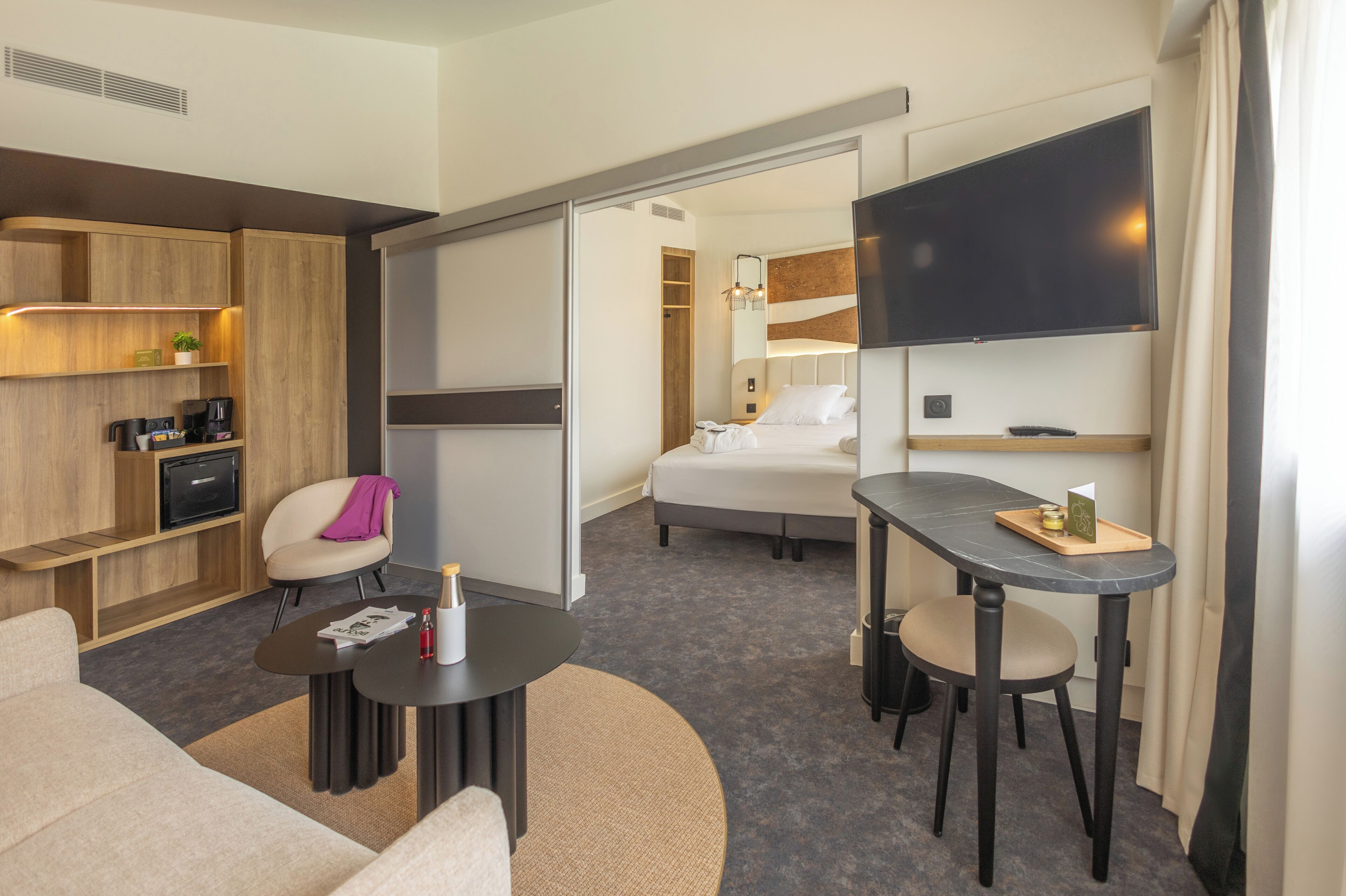 A hotel room with a sofa, a small table, a TV, a bed, and a desk with a chair.