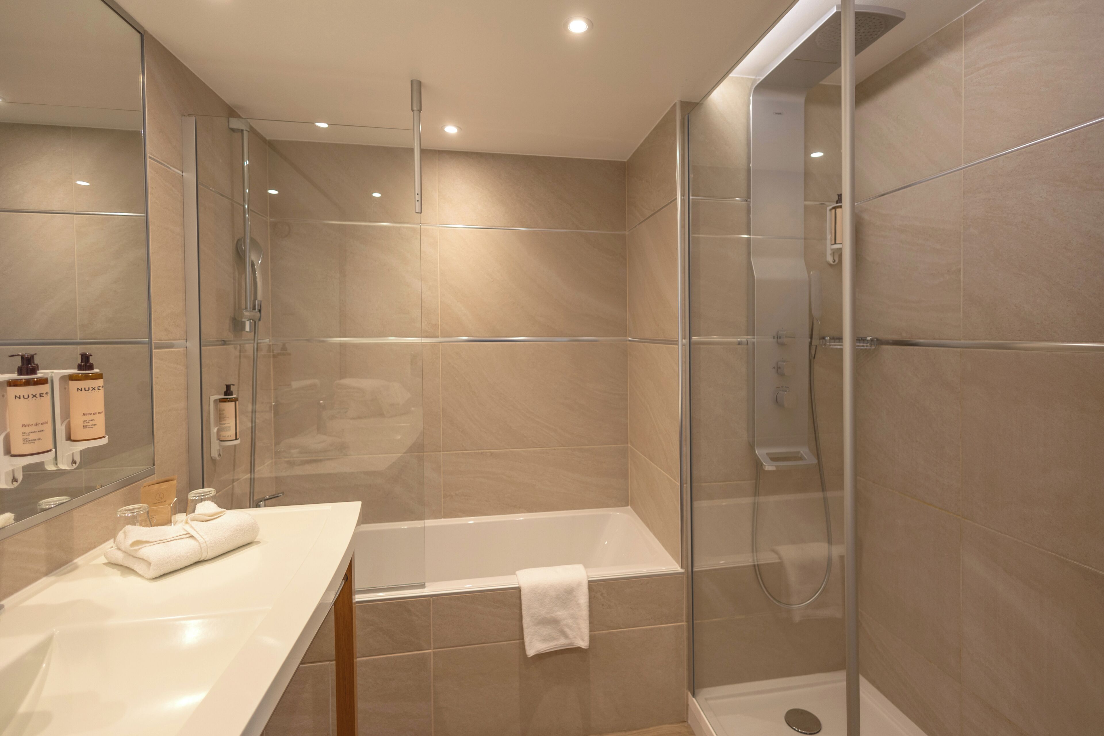 A modern bathroom with a glass-enclosed shower, a white bathtub, and a vanity with toiletries.