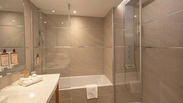 A modern bathroom with a glass-enclosed shower, a white bathtub, and a vanity with toiletries.