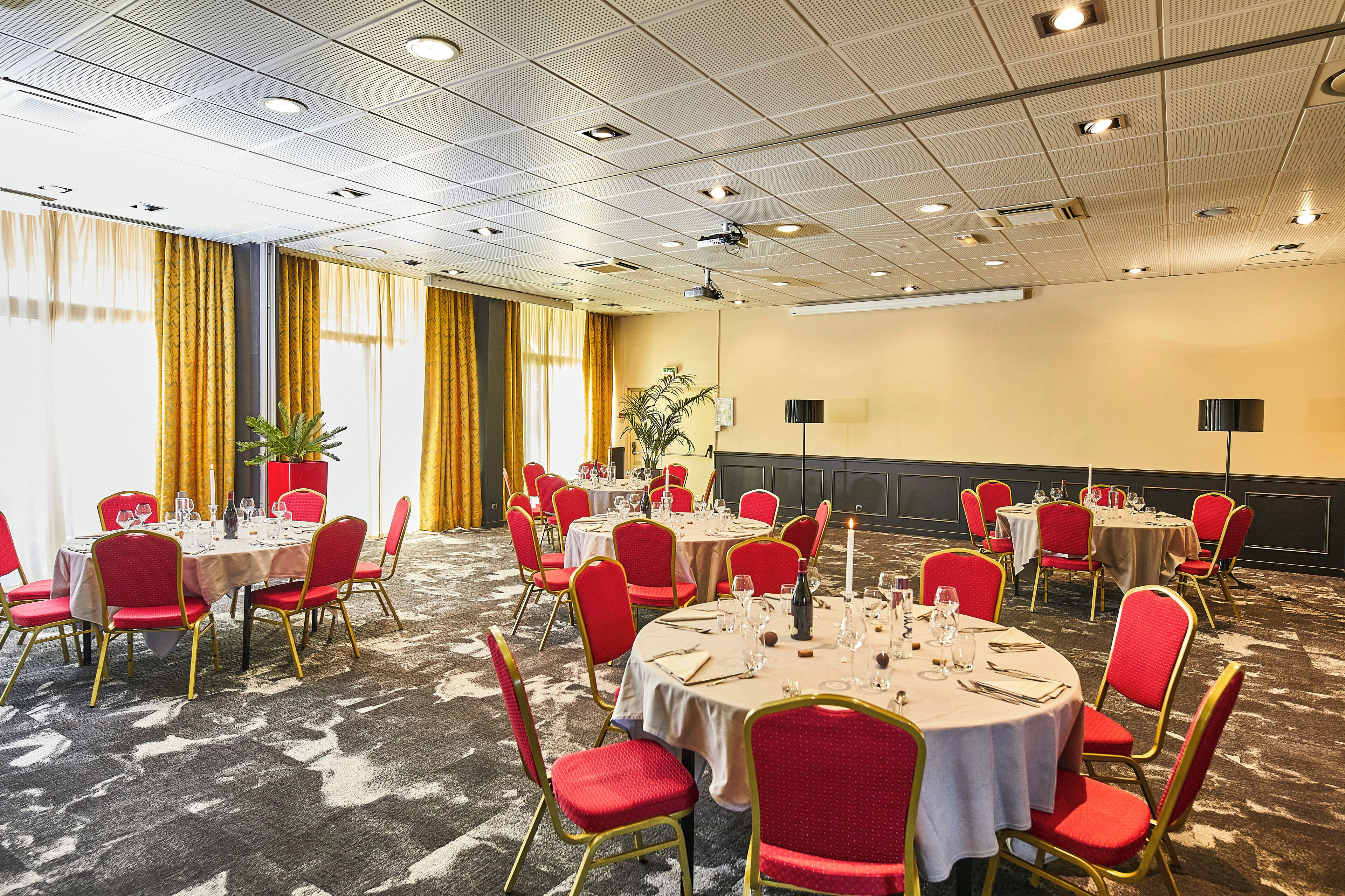 Une salle de conférence dotée de plusieurs tables rondes, de chaises rouges et d’un sol recouvert de moquette.