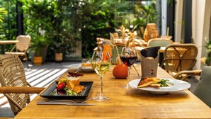 A wooden table with a plate of food, two glasses of wine, and a potted plant in a restaurant setting. - Mercure Beaune Centre (Beaune)