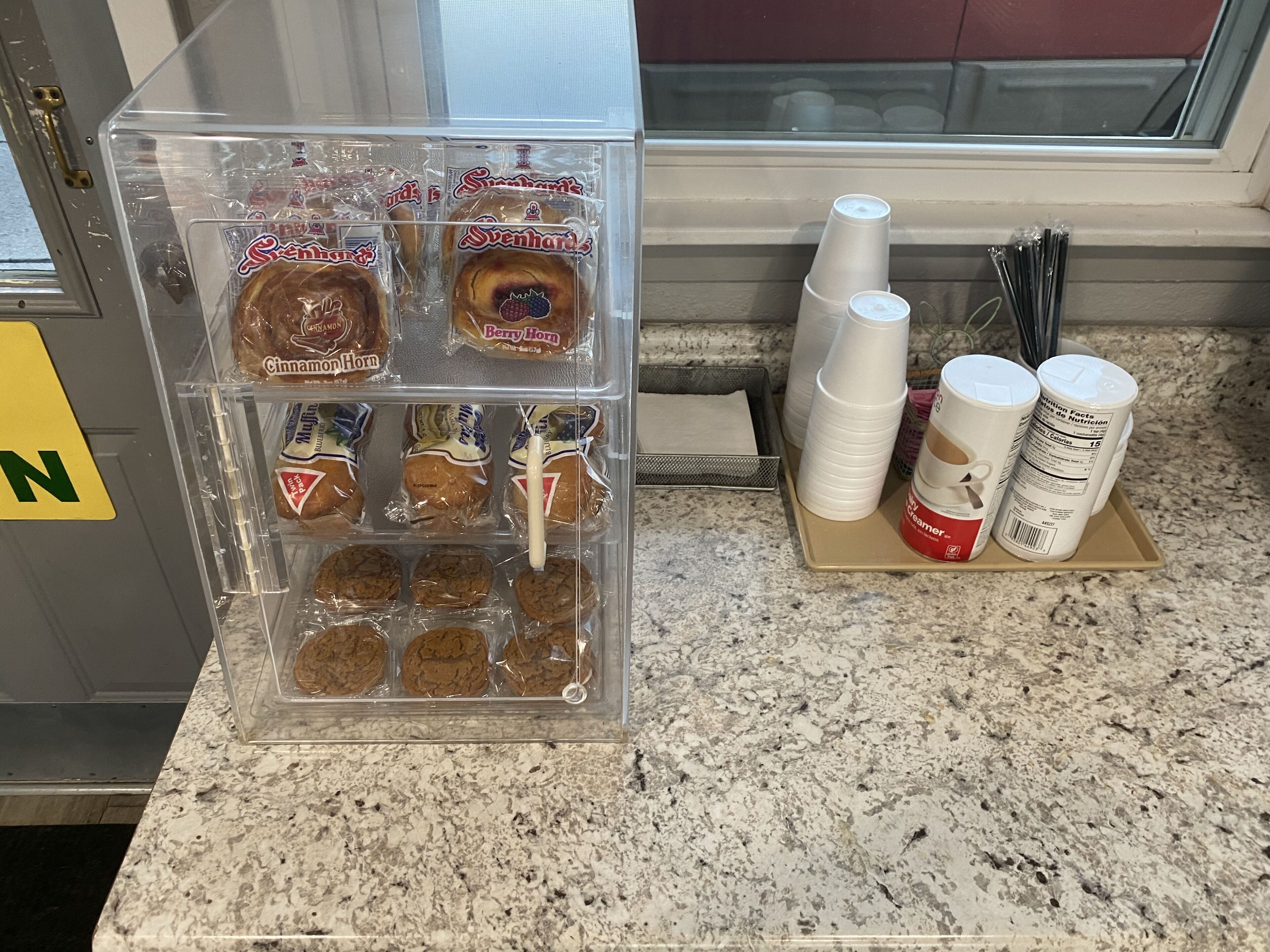 Eine Küchenarbeitsplatte mit einer transparenten Plastikdose, die verschiedene verpackte Snacks enthält, darunter Zimtschnecken und Kekse.