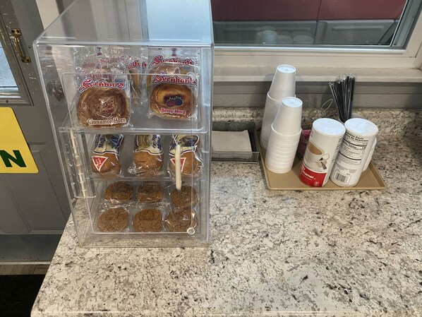 A kitchen counter with a clear plastic container holding various packaged snacks, including cinnamon rolls and cookies.