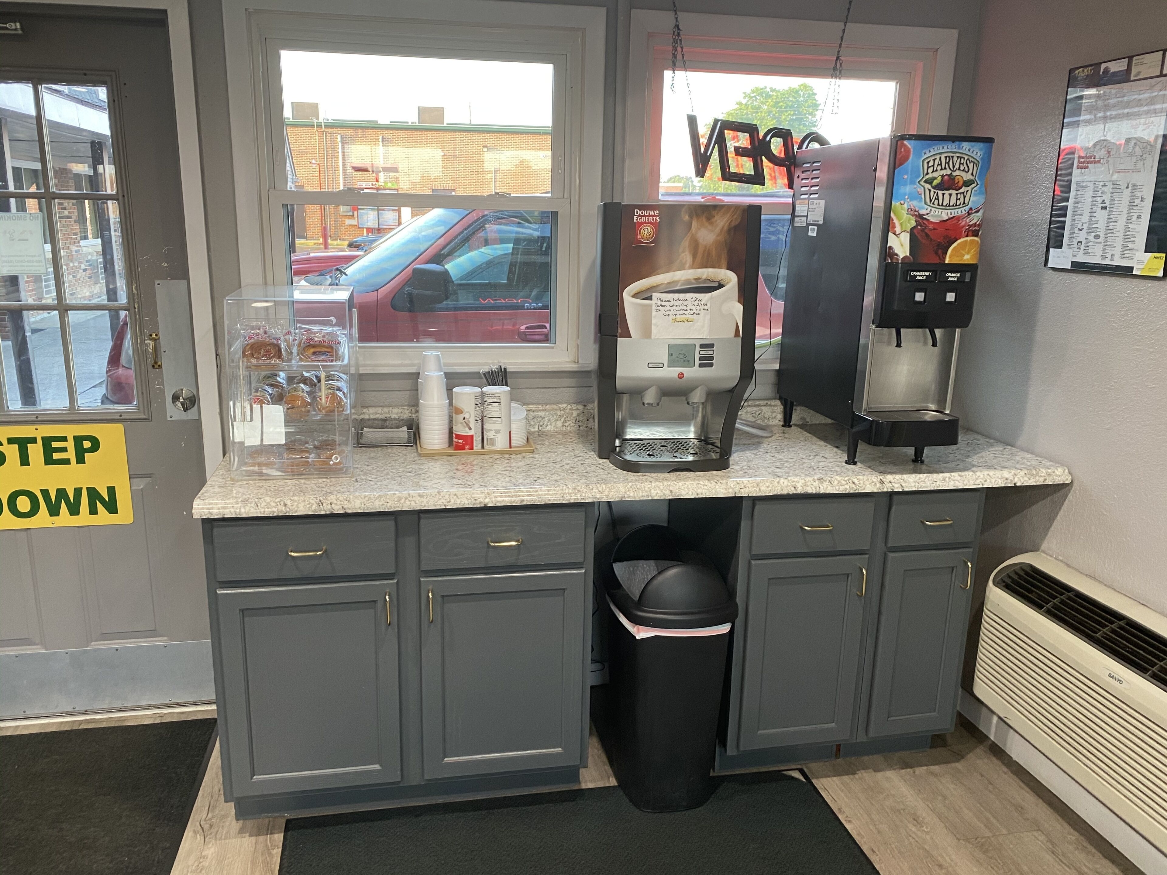 A coffee station with a coffee machine, a beverage dispenser, and a trash bin.