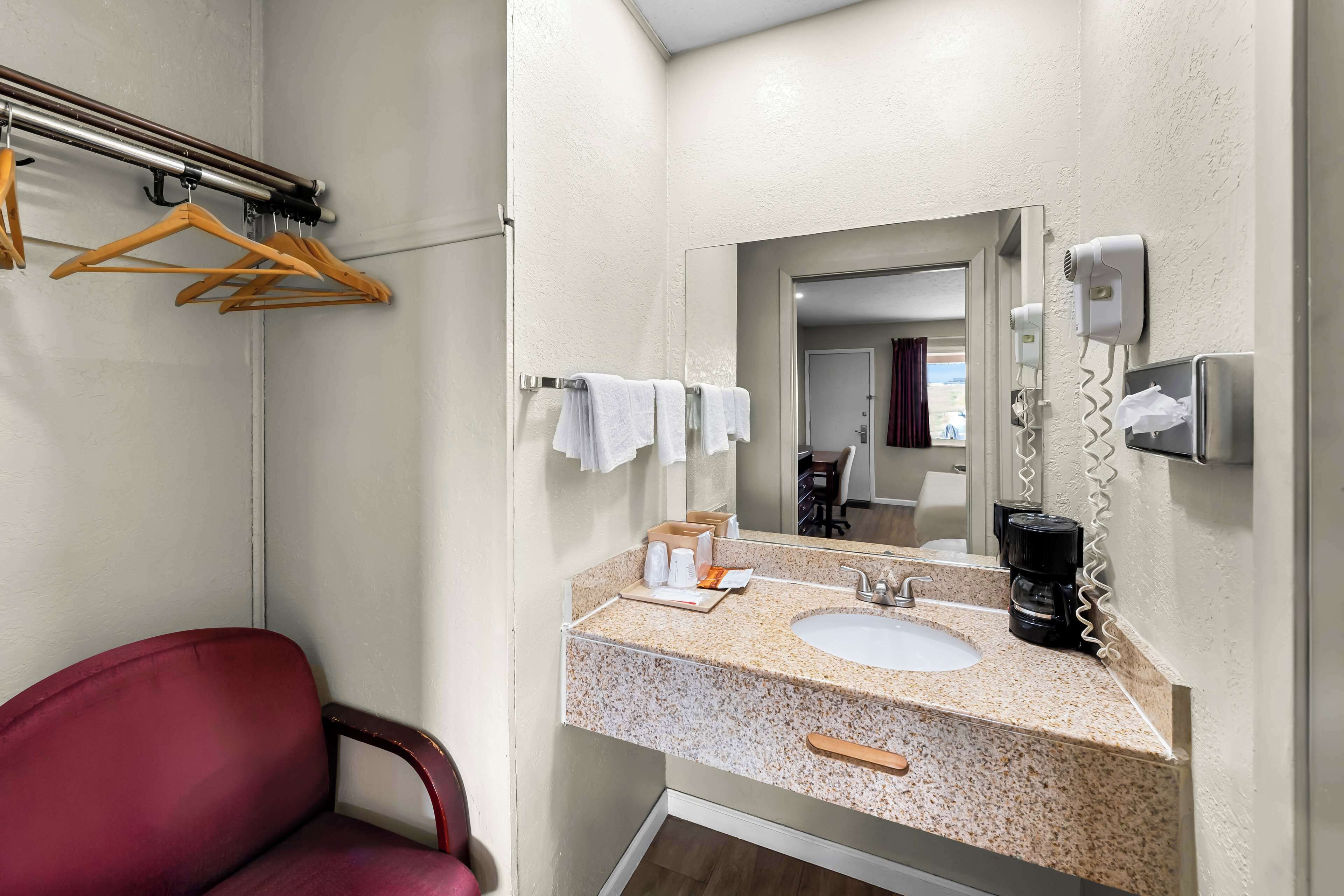 A bathroom with a sink, mirror, towel rack, and a chair.