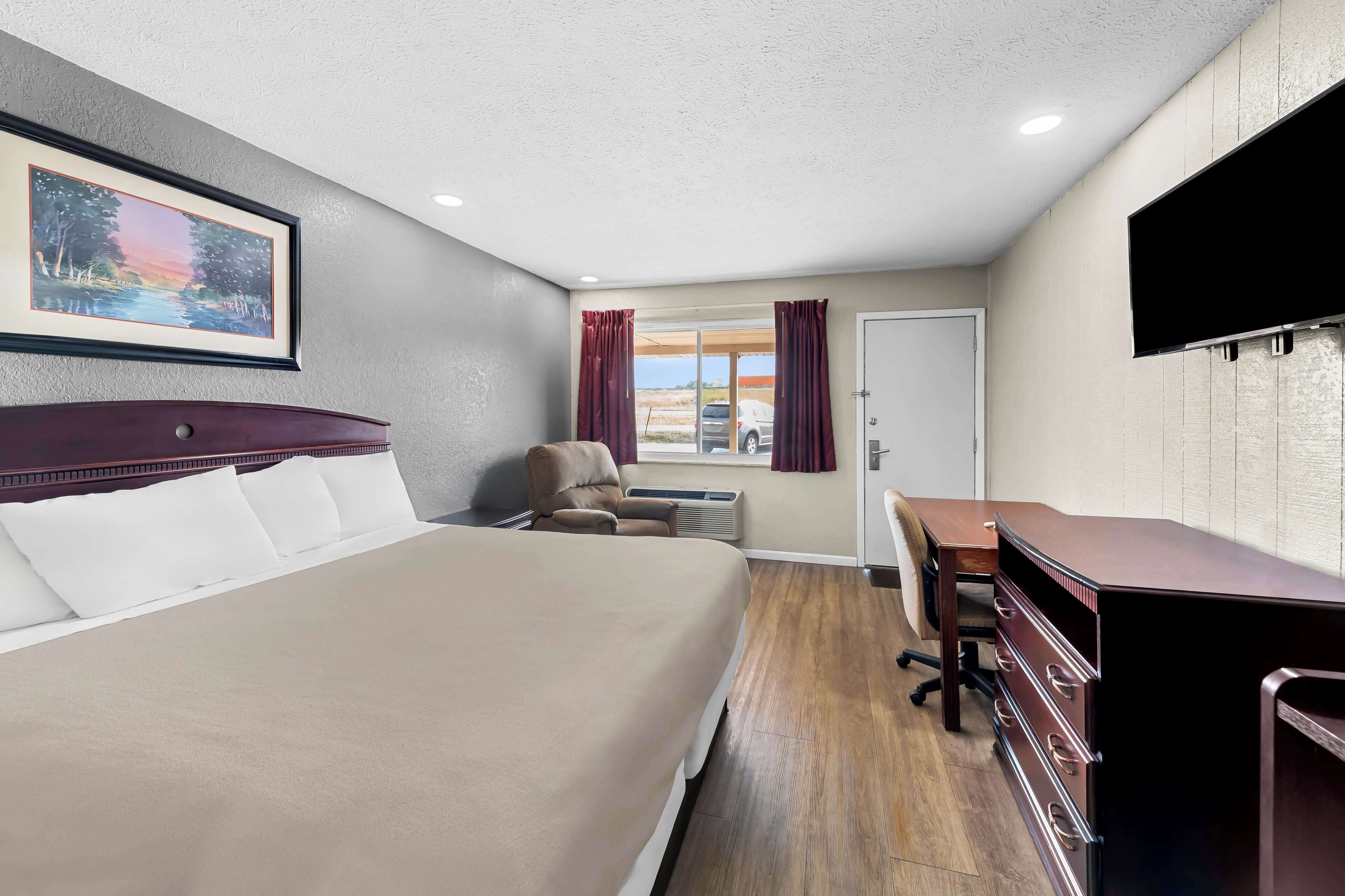 A hotel room with a bed, a desk, a chair, a TV, and a window with curtains.