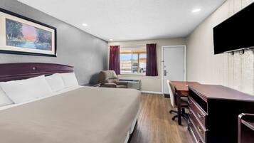 A hotel room with a bed, a desk, a chair, a TV, and a window with curtains.