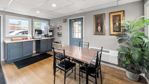 A modern kitchen with grey cabinets, a wooden dining table, and black chairs. There are two framed pictures on the wall, a potted plant, and a window with a view of a car outside. - Americas Best Value Inn Marion, OH (Marion)