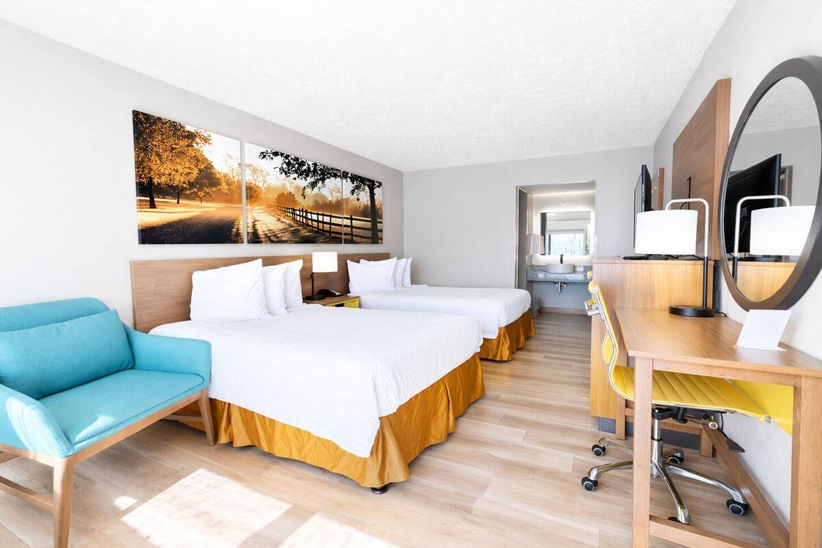 A hotel room with a bed, a desk, a chair, a sofa, and a large painting on the wall.