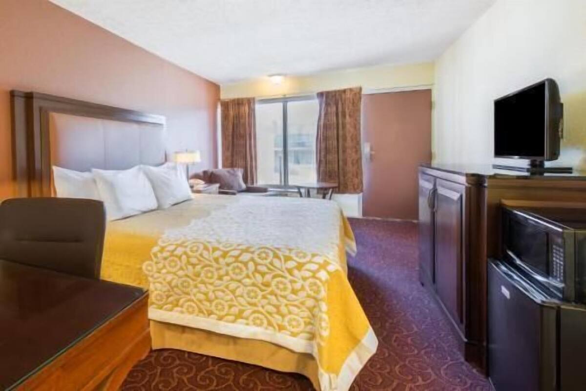 A hotel room with a bed, a desk, a television, and a window.