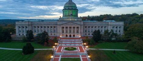 A large government building with a central dome, symmetrical facade, and formal entrance with steps leading to a landscaped garden.