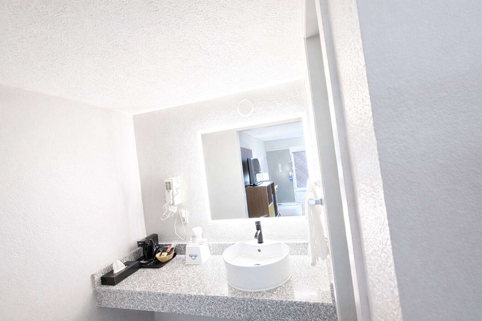 Un baño con lavamanos blanco, un espejo y un perchero para toallas.