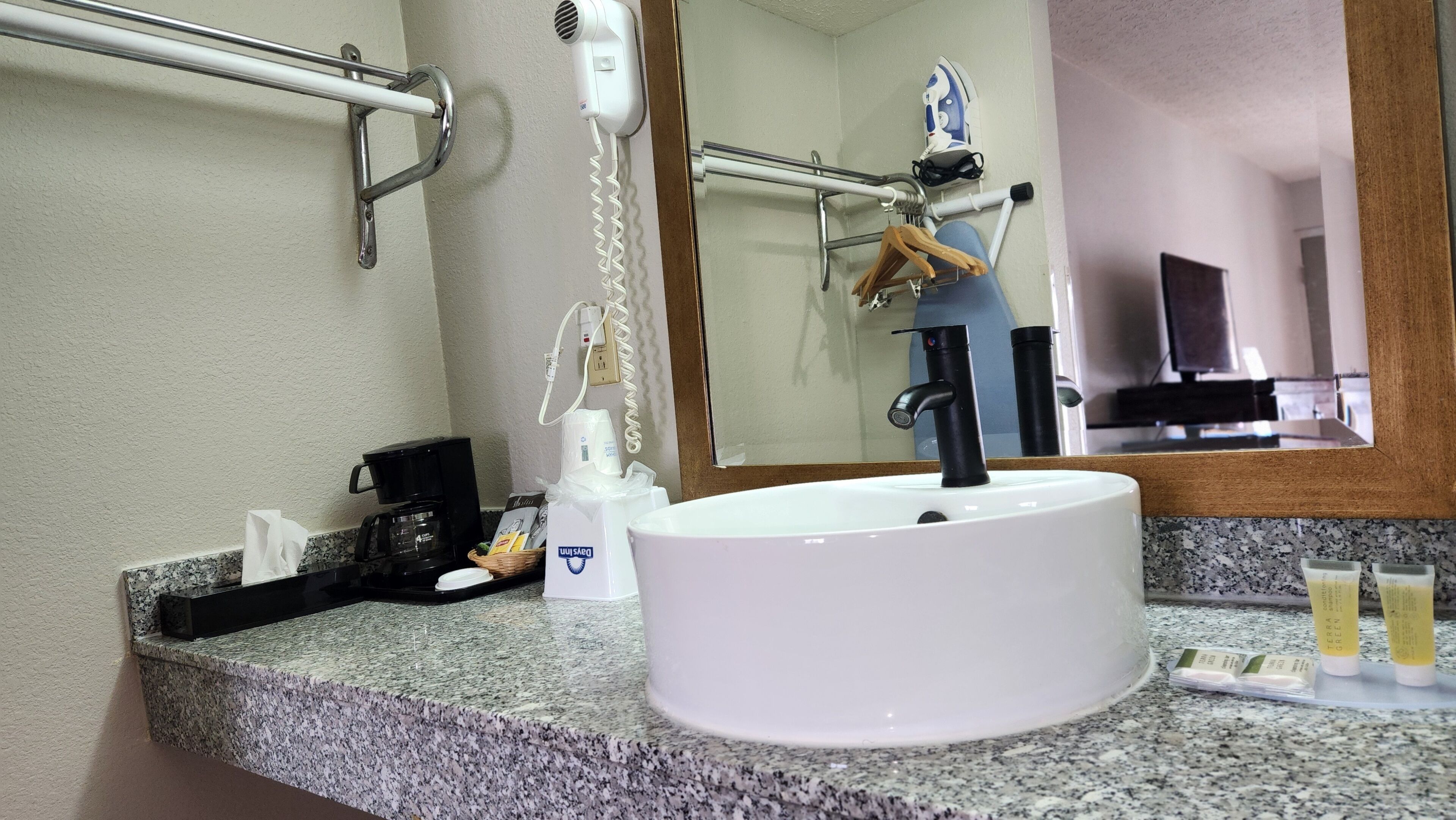 Un bagno con lavandino bianco, uno specchio, un asciugacapelli e una macchina per il caffè.