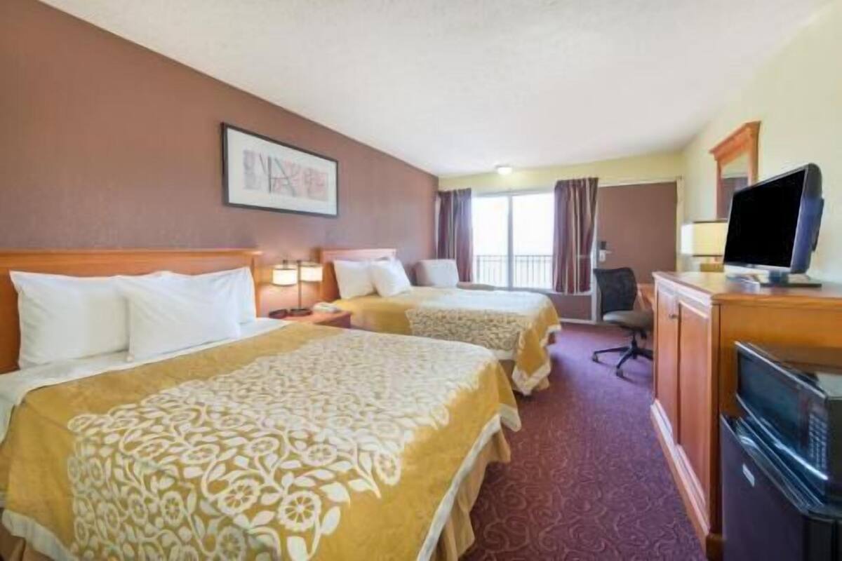 A hotel room with two beds, a television, a desk, and a window with curtains.