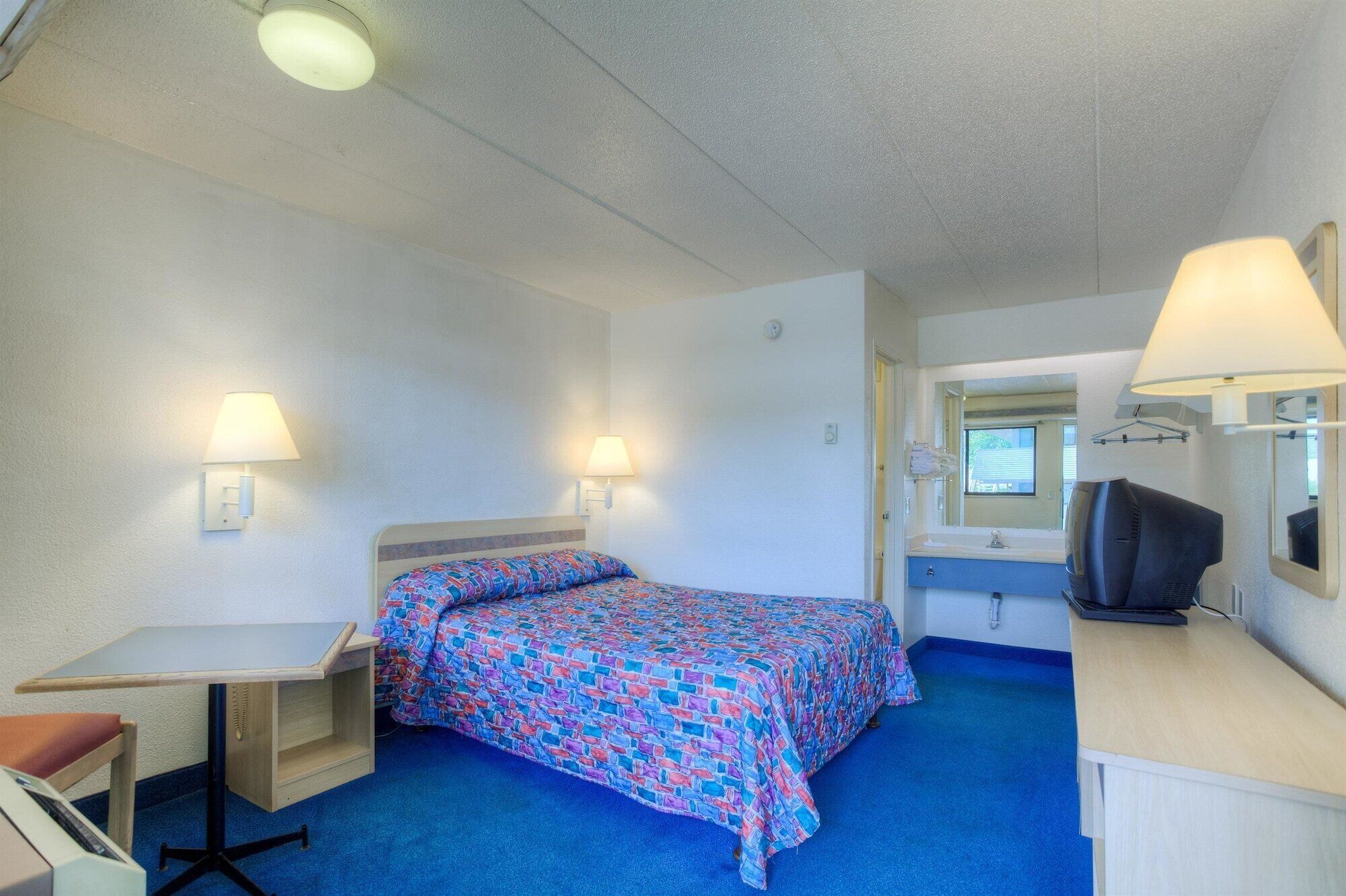 Une chambre d’hôtel de taille modeste, comprenant un lit simple, un bureau, une chaise, une télévision et un miroir.