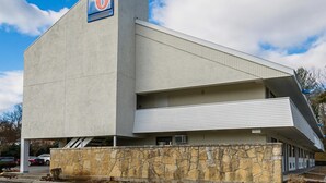 Un moderno motel con un llamativo letrero con el número '6', fachada de piedra y techo plano.