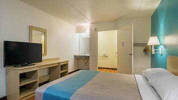 A hotel room with a bed, a TV on a wooden stand, a bathroom with a mirror, and a teal accent wall.
