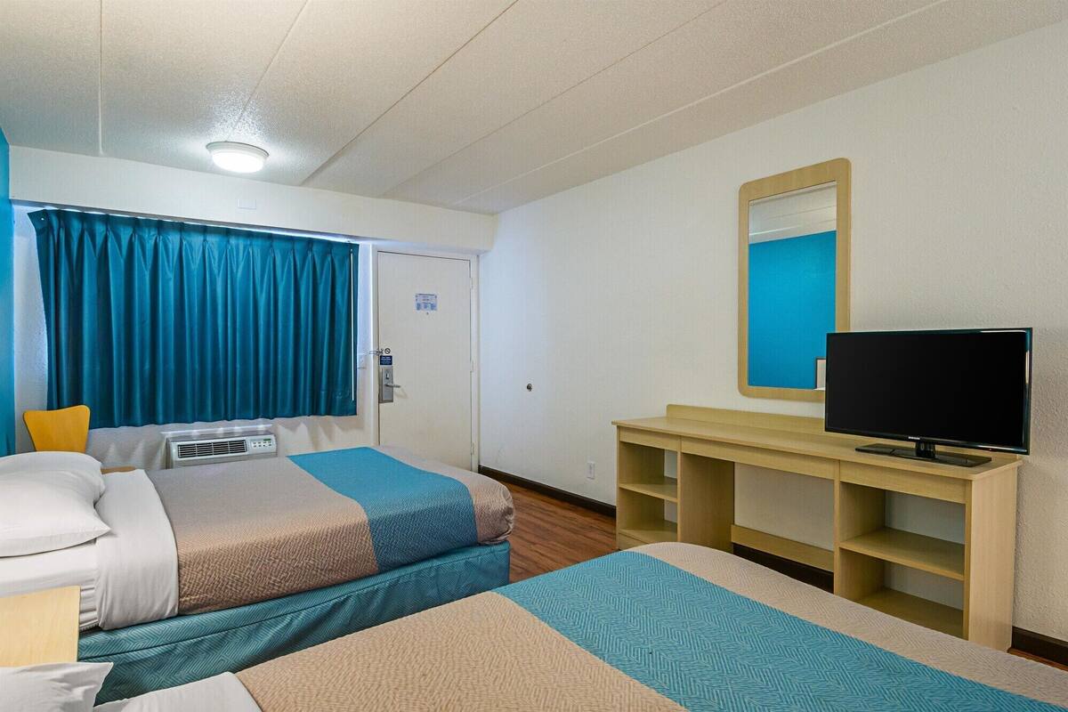A hotel room with two beds, a television, a mirror, and a small desk.