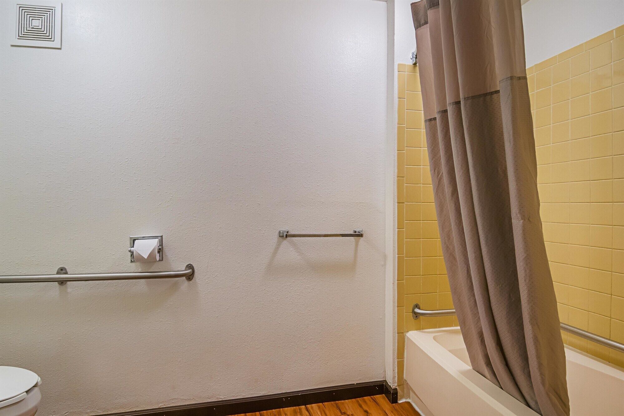 A bathroom with a white toilet, a shower with a brown curtain, and a handrail.