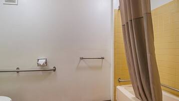 A bathroom with a white toilet, a shower with a brown curtain, and a handrail.
