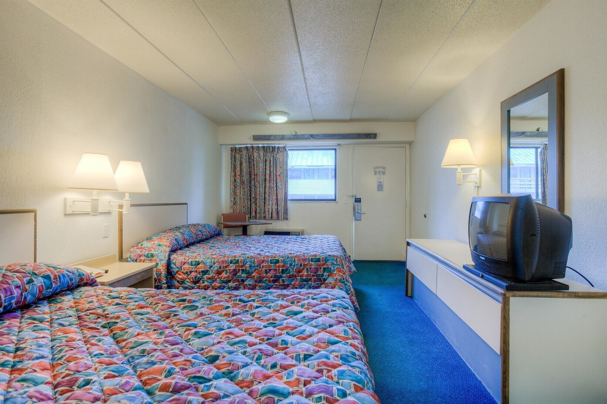 A hotel room with two beds, a television, and a desk.