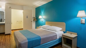 Una habitación de hotel con cama, mesita de noche y lámpara de pared.