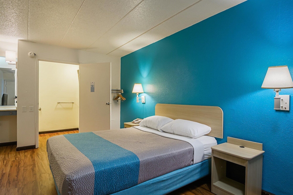 A hotel room with a bed, bedside table, and a wall-mounted lamp.