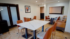 A hotel dining area with marble tables, orange chairs, and a black speaker. - Country Inn & Suites by Radisson, Coeur d'Alene (Coeur d'Alene)