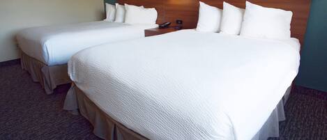 A hotel room with two beds, a wooden headboard, a wall-mounted light, and a carpeted floor.