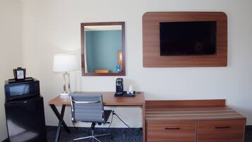 Habitación de hotel con escritorio, silla, televisor, minibar y espejo.