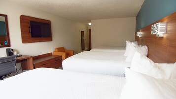 A hotel room with two beds, a desk, a chair, and a TV.