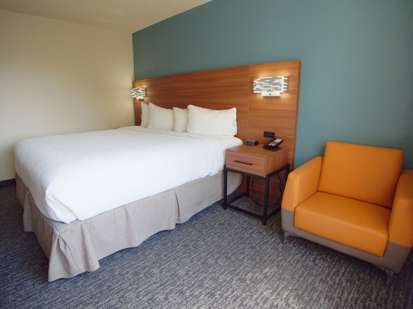A hotel room with a bed, a nightstand with a phone, and an orange chair.