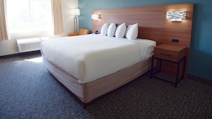 A hotel room with a large bed, a bedside table, a lamp, and a window with curtains. - Country Inn & Suites by Radisson, Coeur d'Alene (Coeur d'Alene)