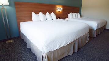 A hotel room with two beds, a nightstand, a lamp, and a wall-mounted light fixture.